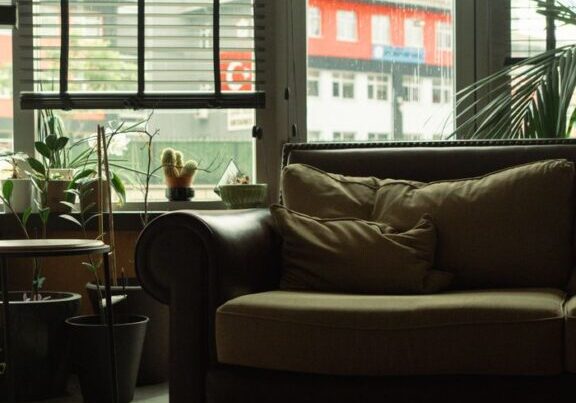 A stylish urban living room with a sofa, potted plants, and large windows.